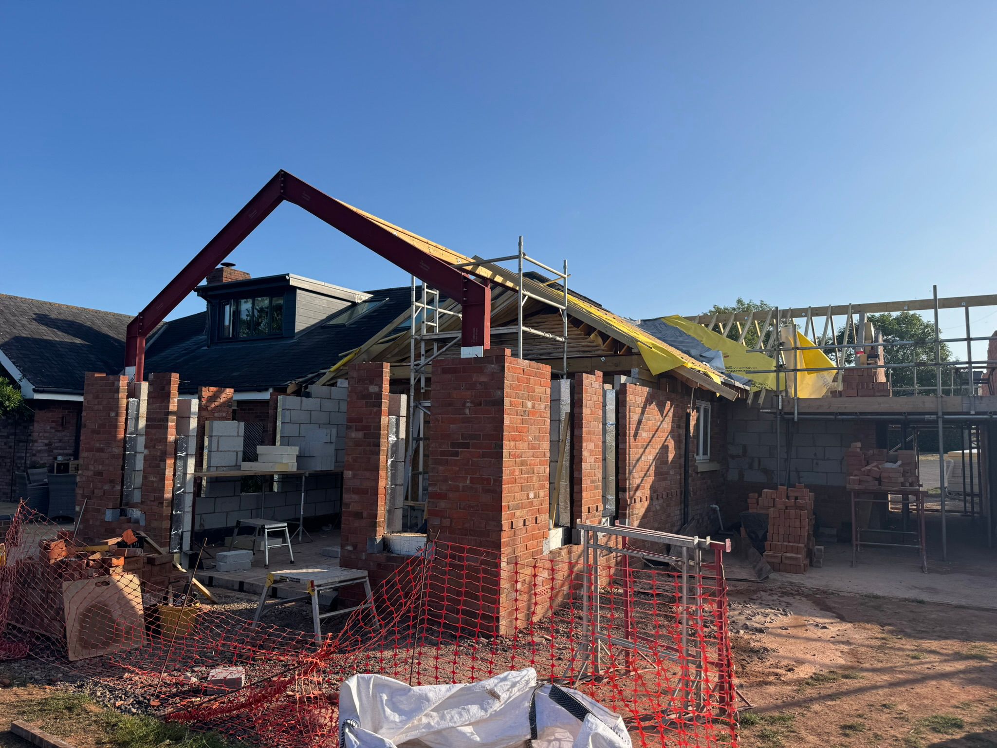 Same extension mid-build with red roof trusses rising and brick walls going up